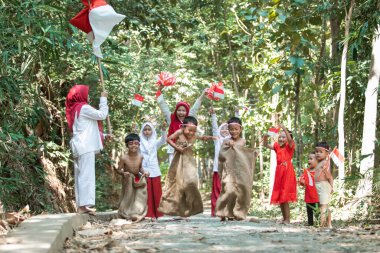 Çocuklar yarışıyor, çocuklar bağımsızlık gününde destekleyici izleyicilerle atlayıp kaçmaya çalışıyor.