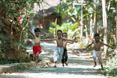 Kırmızı ve beyaz bayrak tutarken kıyafetsiz koşan bir grup çocuğun birbirini kovalaması.