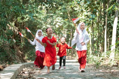 Bir grup küçük kız kırmızı ve beyaz bayrağı tutarken birbirini kovalıyor ve bayrağı birlikte kaldırıyorlardı.