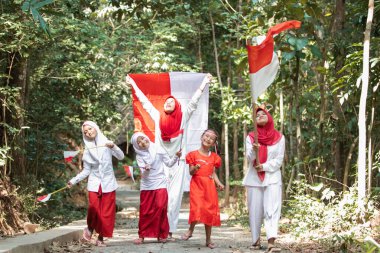 Bir grup Asyalı küçük kız, köy yolunda kırmızı ve beyaz bayrağı tutarken ve kaldırırken kahkahalarla gülüp şarkı söylüyorlar.