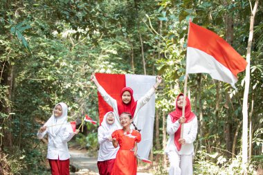 Asyalı küçük kızlar mutlulukla yürür ve kırmızı ve beyaz bayrağı tutarken Endonezya 'nın bağımsızlık gününü kutlamak için bir şarkı söylerler.