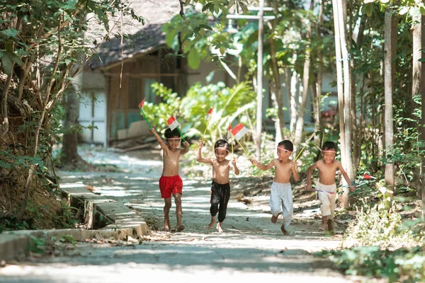 Szórakozás csoport a gyerekek futás ruha nélkül, amikor gazdaság kicsi a piros-fehér zászló, és felemelte a zászlót — Stock Fotó