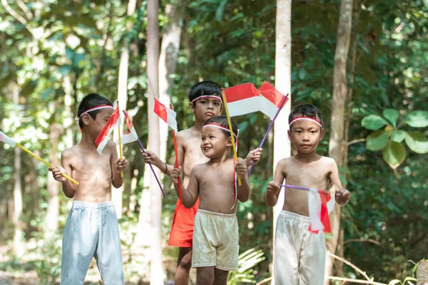 Het hebben van leuke groep kinderen staan zonder kleren bij het vasthouden van kleine de rode en witte vlag en hief de vlag — Stockfoto
