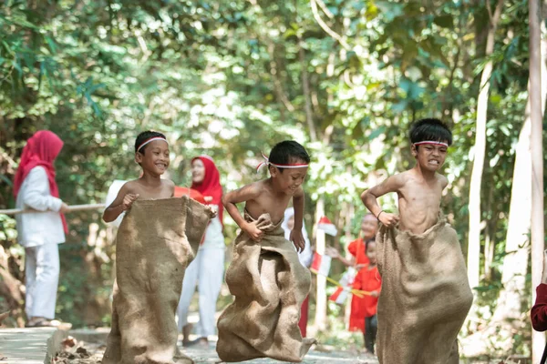 Anak-anak Indonesia mencoba melompat dan berlari di perlombaan karung dengan teman-teman yang mendukung desa — Stok Foto