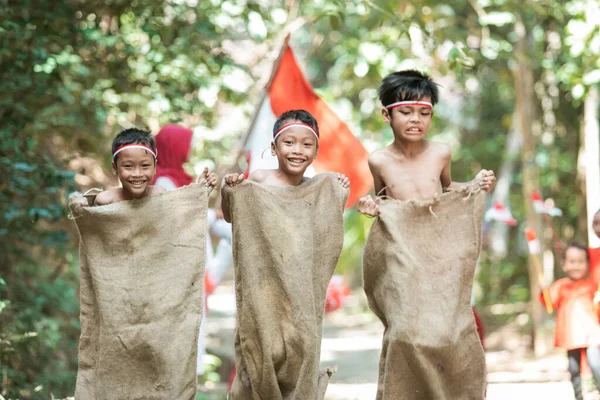 Drie kinderen proberen snel te rennen en springen in de zak race met vrienden hen te ondersteunen — Stockfoto