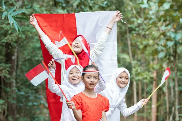 Tersenyum gadis-gadis kecil berdiri dalam barisan ketika memegang dan mengibarkan bendera bersama-sama untuk merayakan hari kemerdekaan Indonesia — Stok Foto