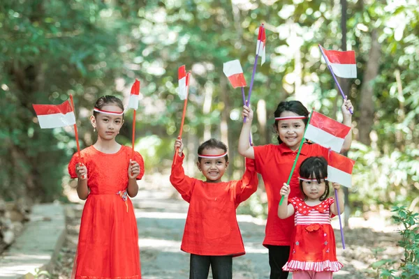 Vier kleine Mädchen lächeln, wenn sie mit rot-weißen Attributen stehen und die indonesische Staatsflagge tragen — Stockfoto