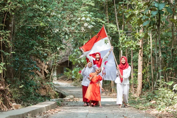 Groupe de petites filles asiatiques marcher avec rire et chanter une chanson lors de la tenue et lever le drapeau rouge et blanc ensemble sur la route du village — Photo