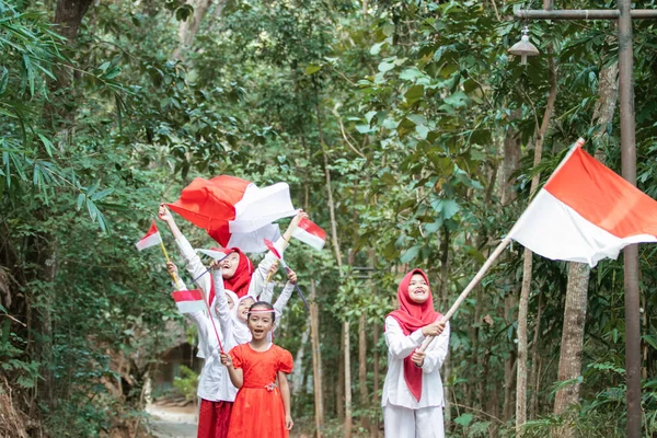 Meninas asiáticas caminhar com felicidade e cantar uma canção quando segurando e levantar a bandeira vermelha e branca juntos para celebrar o dia da independência indonésia — Fotografia de Stock