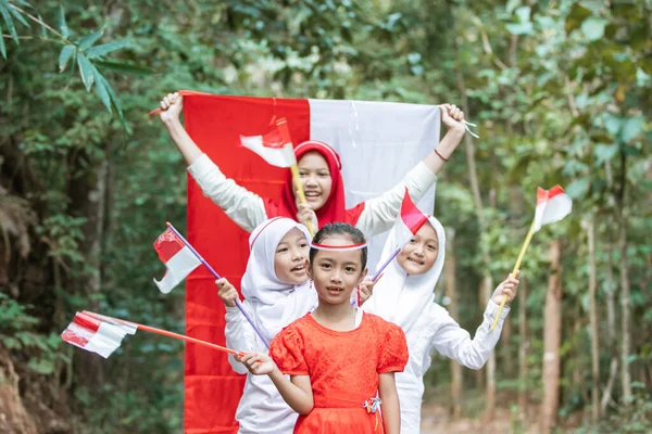Meninas estão em linha com a felicidade ao segurar e levantar a bandeira vermelha e branca juntos para celebrar o dia da independência da Indonésia — Fotografia de Stock