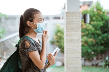 Genç bir öğrencinin portresi. Evin dışında duran bir maske takıyor ve tutuyor.