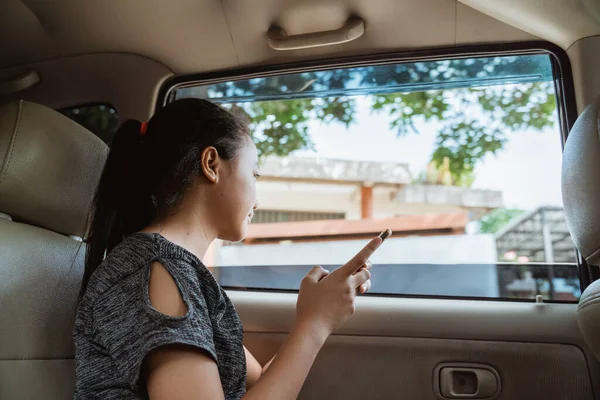 Menina asiática segurando um celular enquanto sentado no carro com a janela aberta — Fotografia de Stock