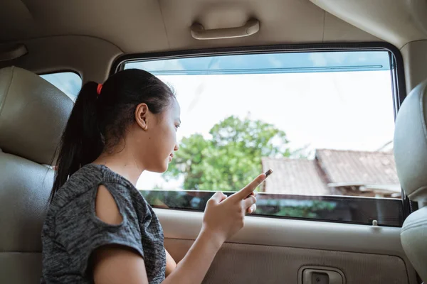 Adolescente menina sorrir quando segurando um smartphone enquanto sentado no carro — Fotografia de Stock