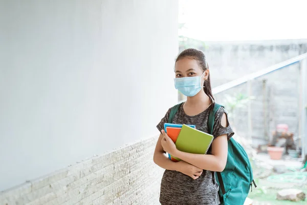 Ein asiatisches Teenager-Mädchen mit Maske und Rucksack, das ein Buch trägt — Stockfoto