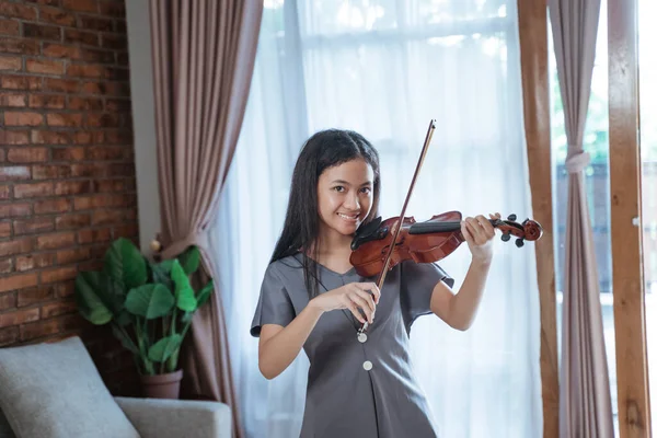 Menina asiática no vestido cinza escuro toca o violino sorrindo enquanto olha para a câmera — Fotografia de Stock