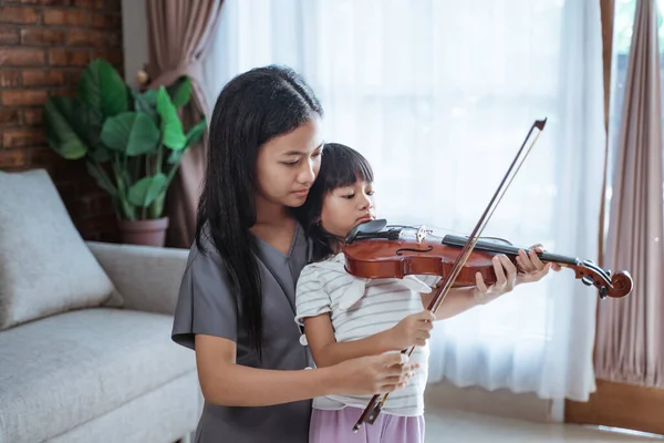 少女在室内拉小提琴时帮助孩子正确地握住小提琴弓 — 图库照片