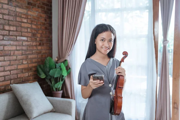 Violinista adolescente sorrindo segurando um telefone celular enquanto estava em uma sala — Fotografia de Stock