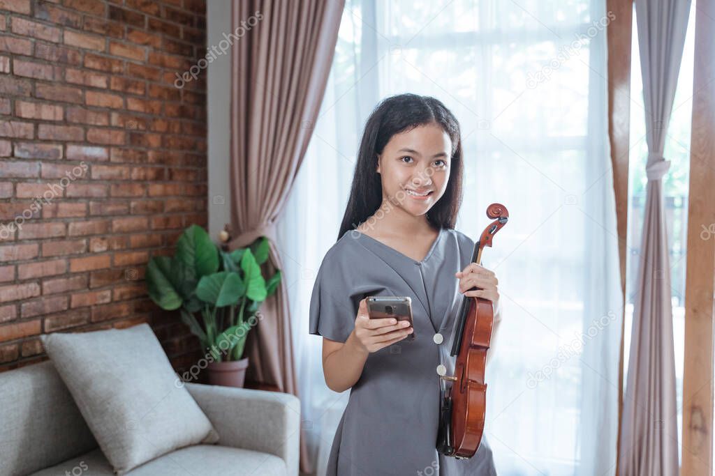 teenage violinist smiling holding a cell phone while standing in a room