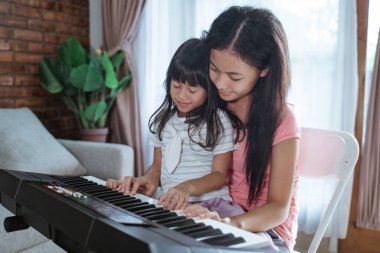 İki Asyalı kız kardeş birlikte oturup piyano çalmaktan zevk alıyorlar.