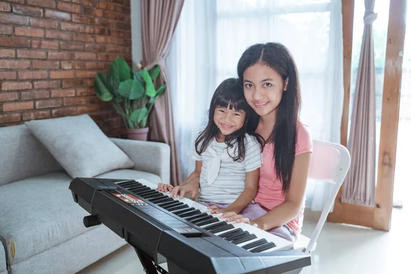 亚洲小女孩和姐姐们喜欢在家里弹钢琴，在大流行期间做一些活动 — 图库照片
