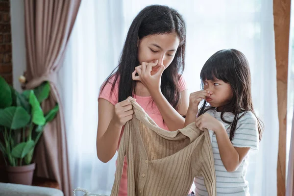 Primer plano de dos hermanas asiáticas cerró la nariz por su dedo al sostener un olor ropa — Foto de Stock