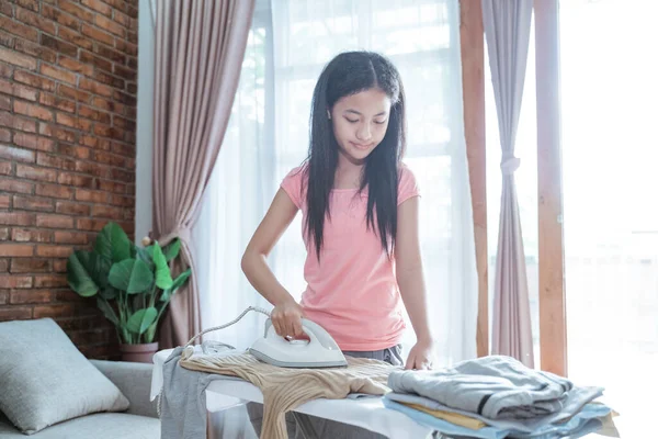 Hermosa chica adolescente planchando ropa para hacer el hogar en la tabla de planchar —  Fotos de Stock