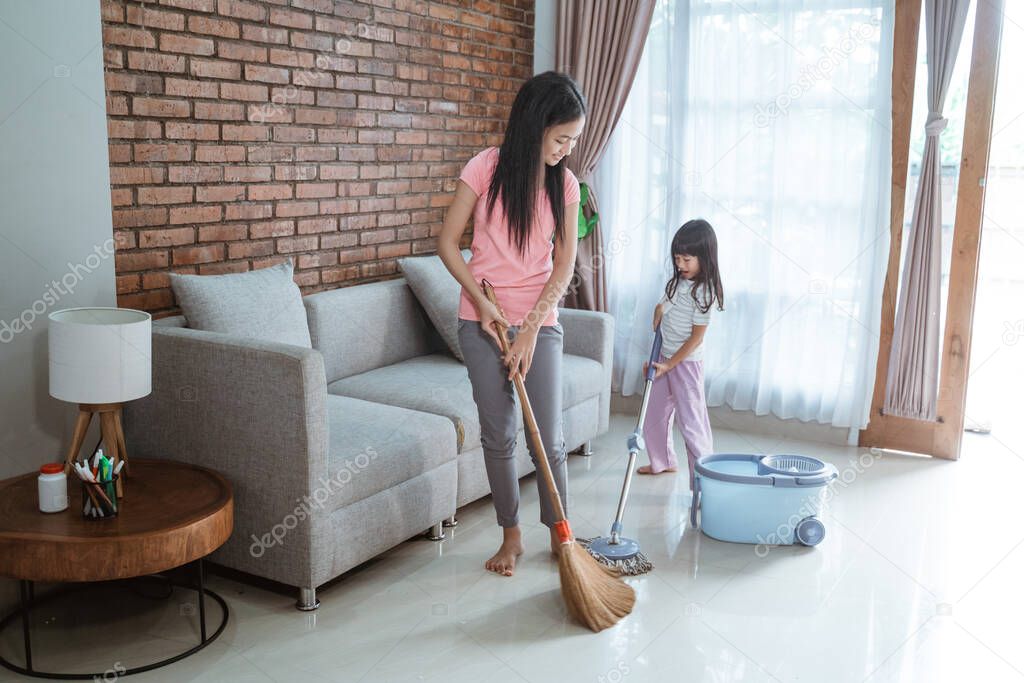 teenage girl holding a broom and little sister holding holding a mop stick