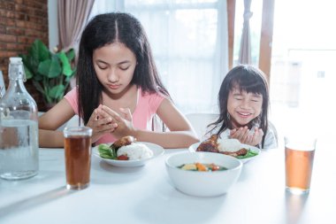 İki kız kardeş yemek masasında birlikte yemek yerken önce dua eder.