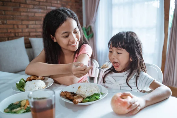 Крупним планом азіатська маленька дівчинка захоплюється їжею, коли її старша сестра годує їжу ложкою, спокушаючи — стокове фото