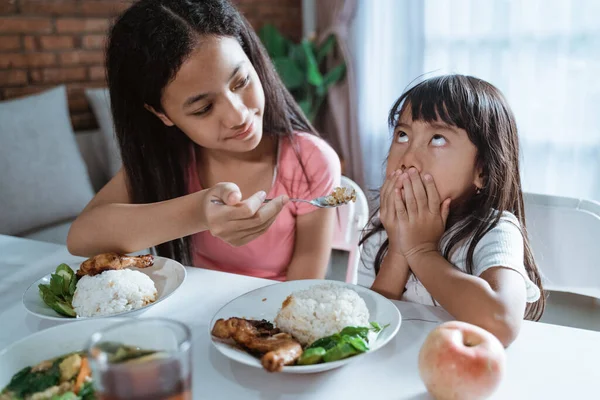 Asiática niña cubrir su boca como su mayor hermana alimentar su comidas —  Fotos de Stock