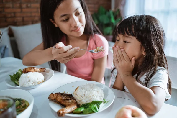 Primer plano de una niña que se cubre la boca no quiere comer cuando su hermana mayor le da de comer con una cuchara — Foto de Stock