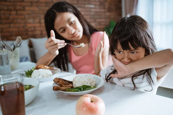 Küçük bir kızın ağzını kapatırken ablası ona kaşıkla yemek yedirirken yemek yemek istememesi. — Stok fotoğraf