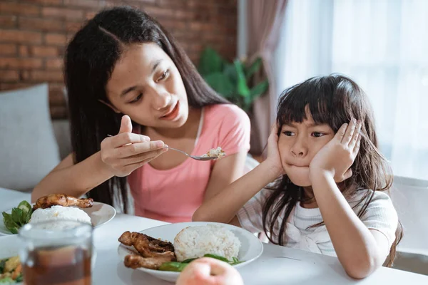 Primer plano de asiático niña se niega a comer cuando su hermana mayor alimentar su comida con una cuchara por seducir —  Fotos de Stock