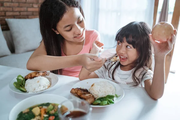 Küçük kız, ablası birlikte yemek yerken onu beslediğinde heyecanlanır. — Stok fotoğraf