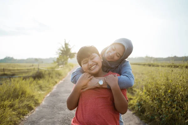 Azji chłopiec uśmiecha się jak jego matka przytula go od tyłu podczas stojąc na drodze — Zdjęcie stockowe