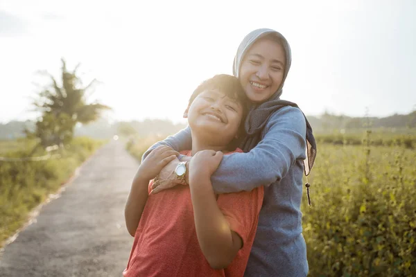 De jongen is blij als zijn moeder knuffelt hem van achteren terwijl hij op de weg — Stockfoto