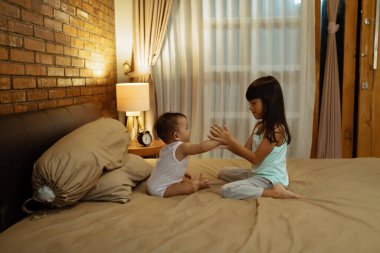 Gülümseyen ve ellerini yatakta çırpan neşeli kardeş imajı.