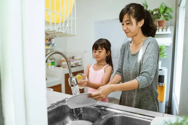Маленька дівчинка допоможіть мамі мити посуд — стокове фото