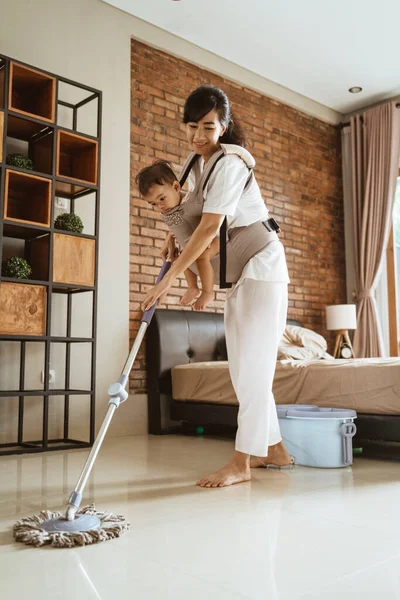 Portrait of a woman carries her baby mopping bedroom floor — Stock Photo, Image