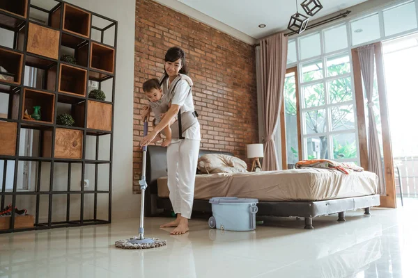 Portrait of a woman carries her baby mopping floor — Stock Photo, Image