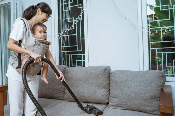 Mother with vacuum cleaner holding her baby on hands — Stock Photo, Image