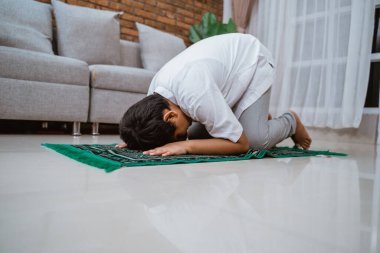 Koko tişörtü giyen Asyalı Müslüman çocuk eğilip dua ediyor.