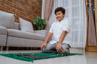 Koko tişörtü giymiş neşeli Asyalı Müslüman çocuk dua ediyor.