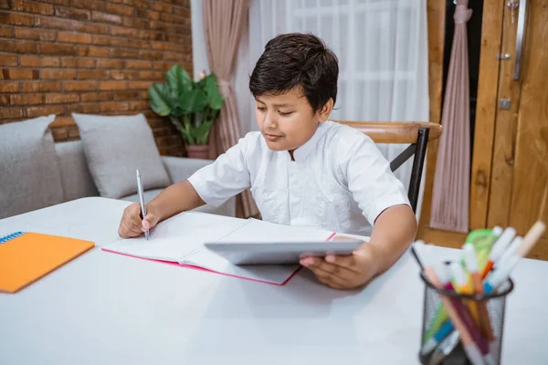 Anak laki-laki berkonsentrasi pada menulis di notebook dan menggunakan tablet digital — Stok Foto