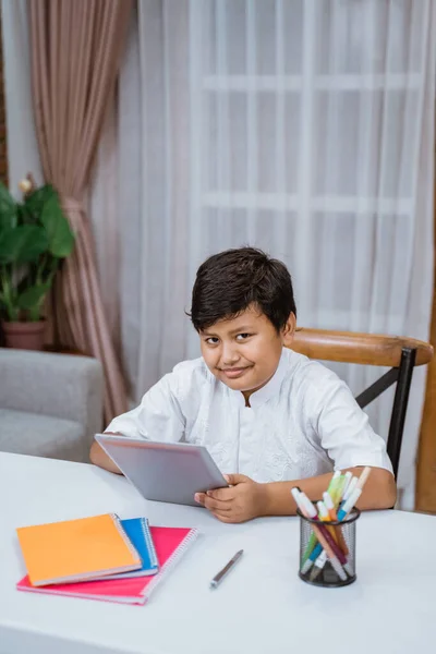 Smiling boy using a tablet doing schoolwork on the desk — Stock Photo, Image