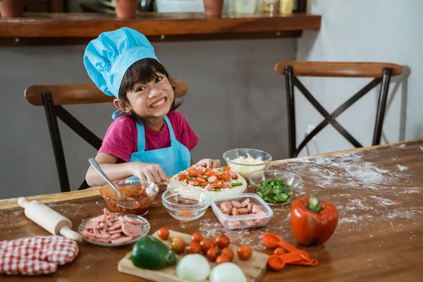 Mavi önlüklü küçük kız lezzetli ev yapımı pizza için pizza kabuğu yapıyor. — Stok fotoğraf