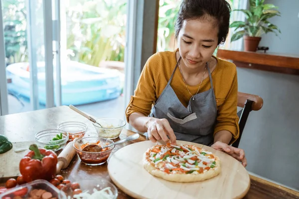 Молодая взрослая женщина домохозяйка пекарь носить фартук делает домашнюю пиццу на кухонном столе — стоковое фото