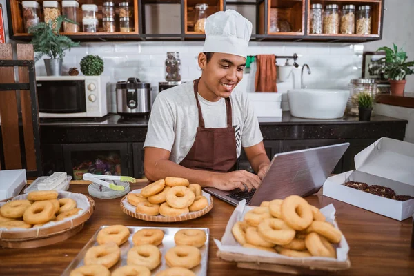 Шеф-повар использует ноутбук для продажи домашних пончиков — стоковое фото