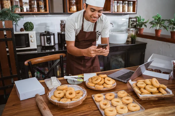 Samec kuchař se usmívá při focení koblih pomocí smartphonu — Stock fotografie