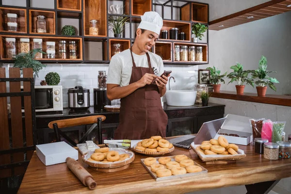 Шеф-повар улыбается, используя свой смартфон для онлайн-маркетинга — стоковое фото
